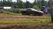 1979 Ford Bronco - A red sports car appears to be stuck in a muddy field with its wheels removed.