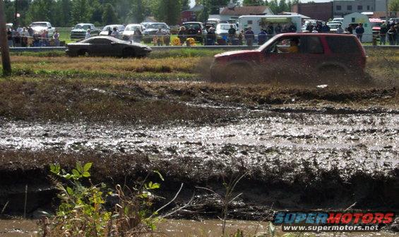 Red SUV splashing through mud pit