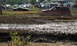 1979 Ford Bronco - A red SUV navigates a muddy obstacle course, kicking up water and dirt.