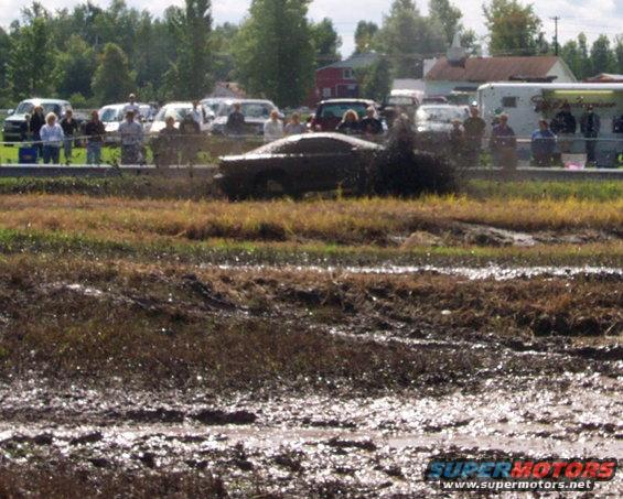 Car stuck in mud pit with spectators watching