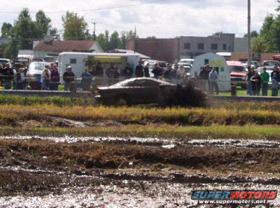 Muddy car driving through a mud pit with spectators watching