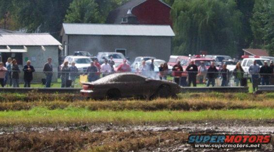 Car covered in mud, stuck in a muddy field with spectators watching