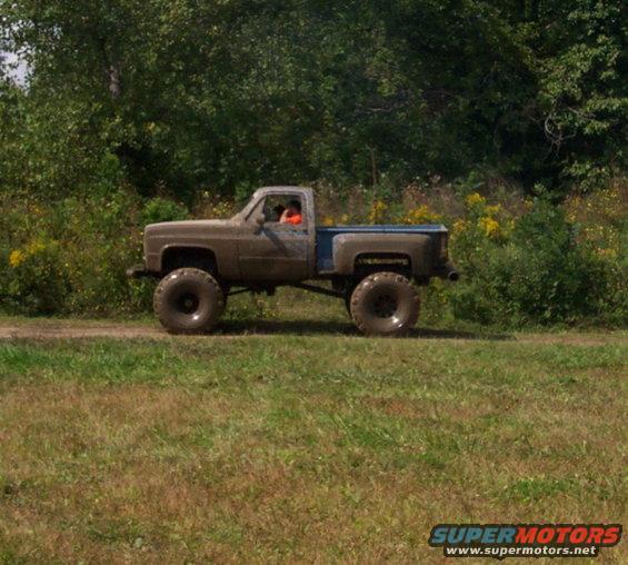 Brown and blue lifted pickup truck with large tires driving on a dirt road