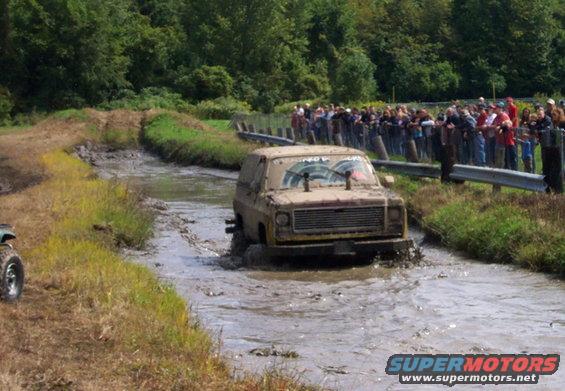 Off-road vehicle driving through mud pit with spectators watching