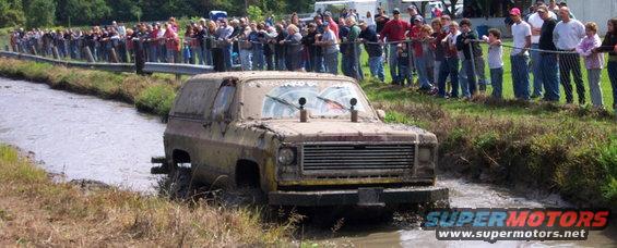 Muddy SUV navigating a mud pit with spectators watching