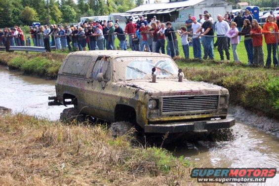 1979 Ford Bronco driving through mud, front grille visible, crowd watching