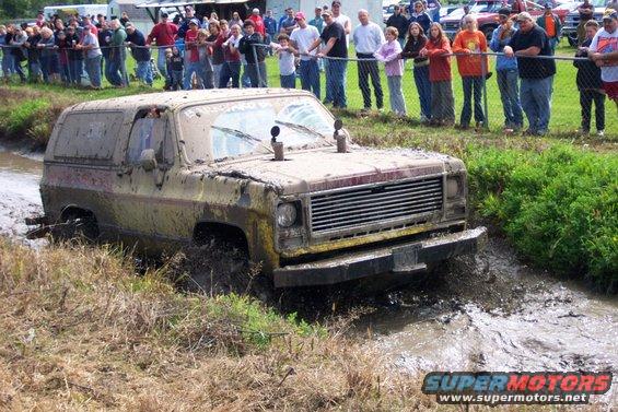 Muddy SUV stuck in a ditch with spectators watching