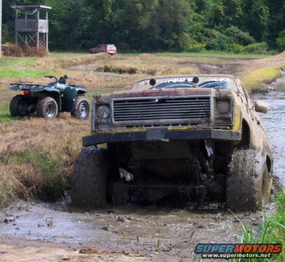 Mud-covered truck stuck in mud, with an ATV nearby