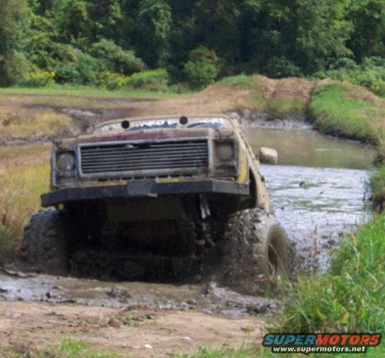 Modified off-road truck with large tires driving through a muddy water obstacle