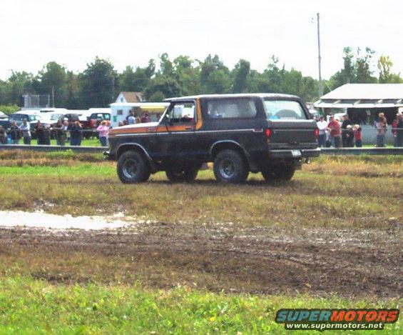 Black Ford Bronco with orange stripe driving through mud, spectators in background