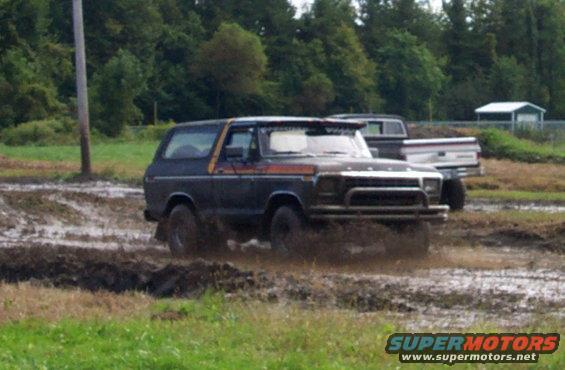 Dark blue 1978 Ford Bronco with orange stripe driving through mud