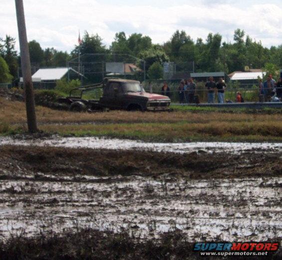Red pickup truck with a bare chassis stuck in mud, front grille visible