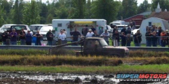 Mud-splattered pickup truck in a muddy field with spectators watching