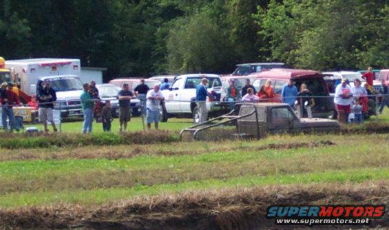 Mud bogging event with a truck stuck in the mud and spectators watching
