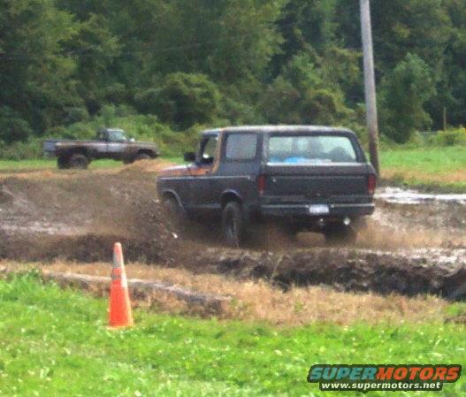 Dark Ford Bronco driving through mud, another truck in background