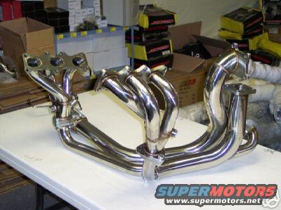 Chrome exhaust manifold on a white table, with boxes in the background