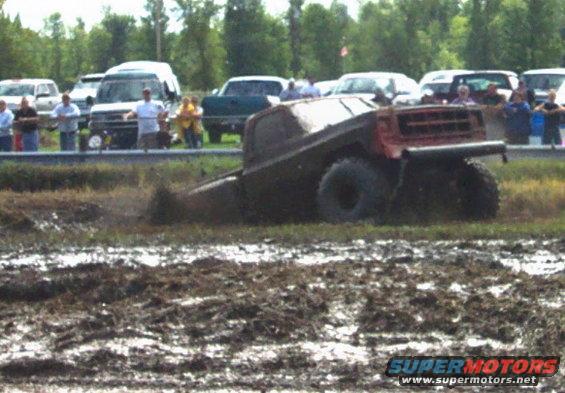 Muddy truck stuck in a bog with people watching