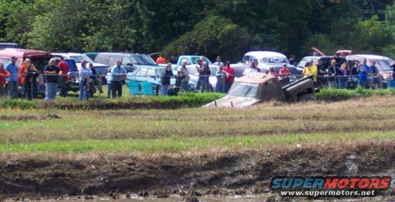 Truck stuck in mud pit with spectators watching from the side