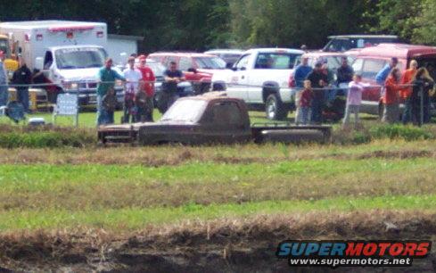 Brown pickup truck partially submerged in muddy grass, side view