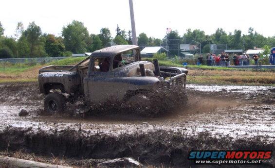 Mud-splattered pickup truck driving through a mud bog