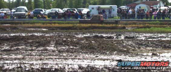 Truck driving through a mud bog with spectators in the background