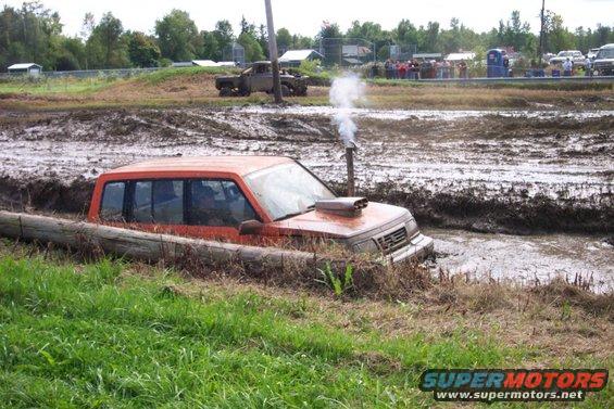 Orange SUV with snorkel exhaust stuck in mud pit, log in foreground