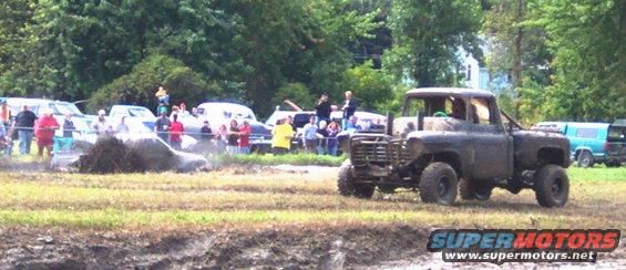 Muddy truck in a field with spectators watching a vehicle stuck in the mud