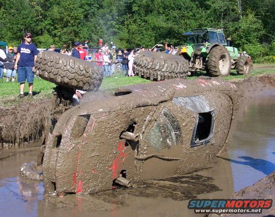 Mud-covered vehicle stuck in mud pit, tractor in background