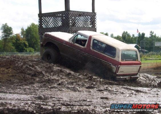 Red and white 1979 Ford Bronco navigating a muddy hill