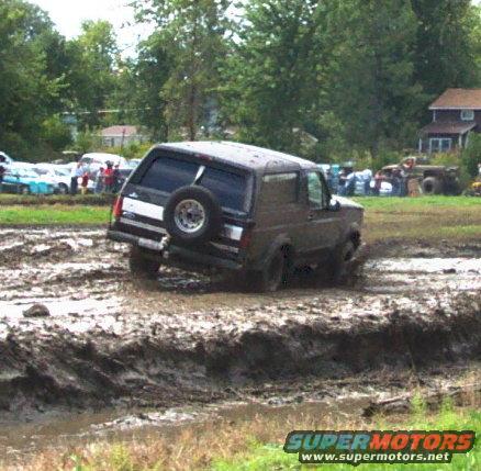 Dark brown Ford Bronco with spare tire on rear door driving through a mud pit