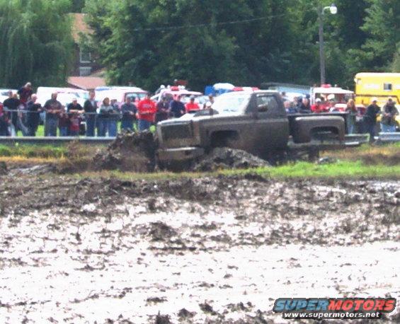 Truck stuck in mud pit with spectators watching
