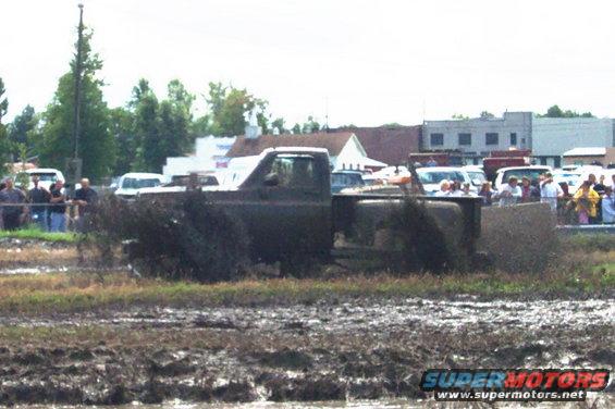Mud-splattered dark pickup truck driving through a muddy field