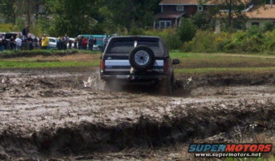 Black SUV driving through mud, spare tire on rear