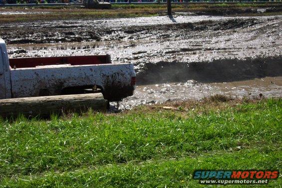 Muddy pickup truck stuck in a mud pit, with water splashing