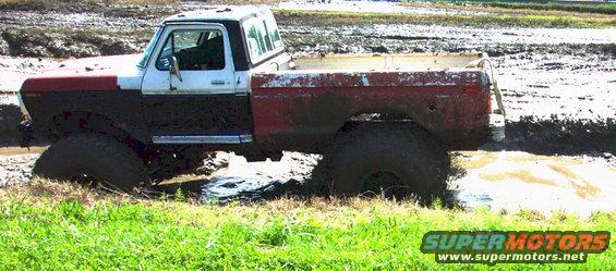 Mud-splattered 1978 Ford Bronco with red and white body stuck in mud, side view