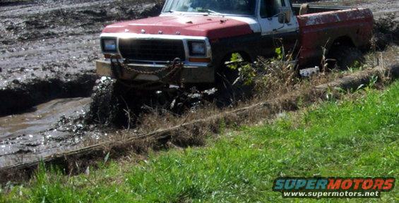 Red and white pickup truck stuck in mud, 3q-front view
