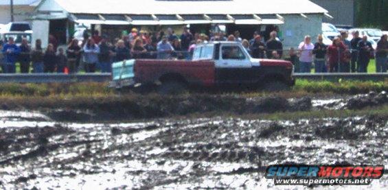 Red and white pickup truck with a teal bed stuck in mud, side view