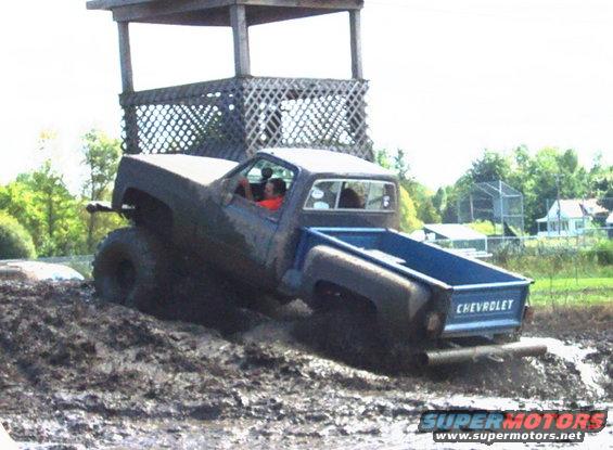 Chevrolet pickup truck driving through mud near a wooden structure