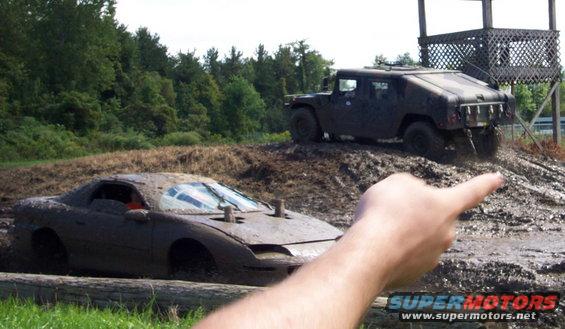 Mud-covered sports car stuck in mud, Humvee in background