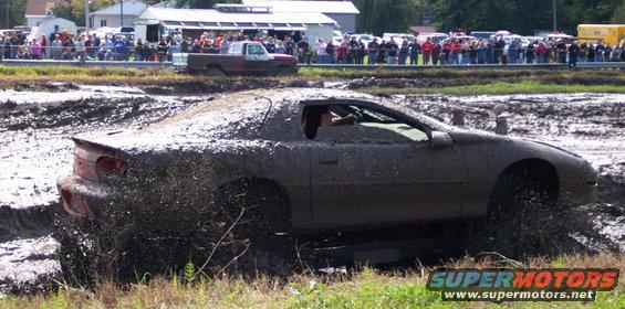 Mud-covered sports car splashing through a mud pit