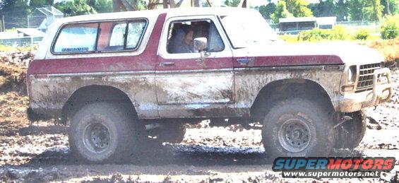 Red and white Ford Bronco with mud splatters, seen from the front-right angle in a muddy terrain