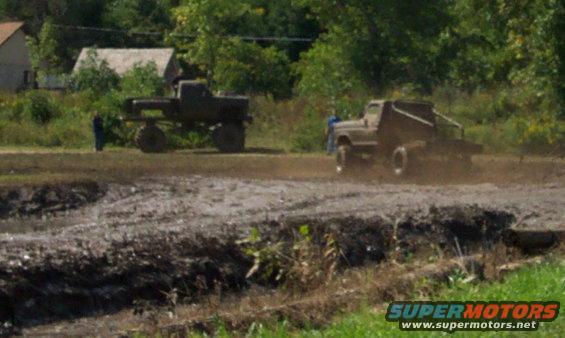 Two trucks driving through a mud pit