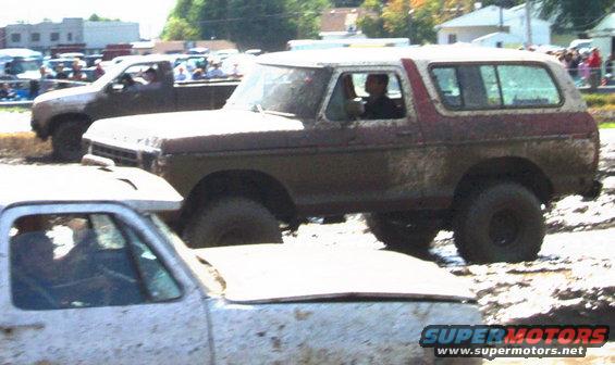 Mud-covered red and white 1978 Ford Bronco in a mud bog, viewed from the front-right