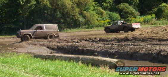 1979 Ford Bronco and pickup truck driving through mud on an off-road course