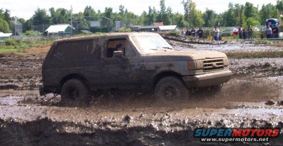 Muddy SUV driving through a mud pit, splashing mud