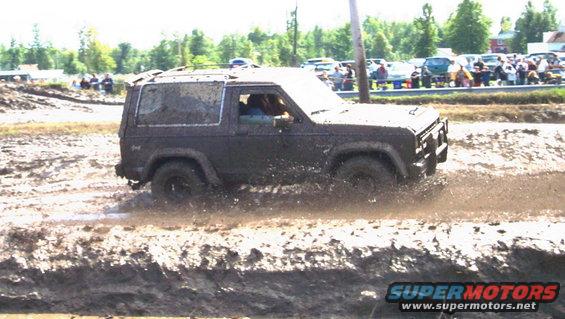 Mud-covered dark SUV driving through a mud pit, side view