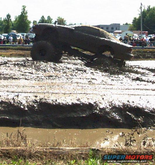 Mud covered truck driving through a mud pit with spectators in the background