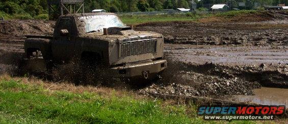Muddy pickup truck splashing through a mud pit