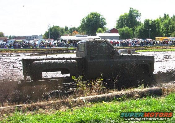 Mud-covered pickup truck stuck in a mud bog with spectators in the background