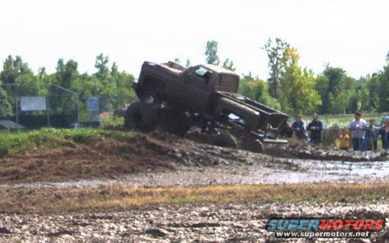 Muddy truck stuck in a bog with people watching